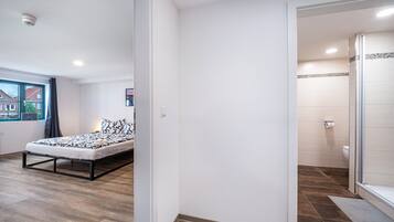 Un dormitori amb un llit, una finestra amb vistes, un bany amb dutxa i una porta que condueix a una altra habitació.