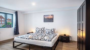Un dormitorio con cama, mesita de noche, un cuadro en la pared y ventana con cortinas.