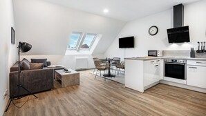 A modern apartment with a loft-style ceiling, a kitchenette, a dining area, and a living space with a sofa and coffee table. - Modern apartment in the city center of Jever (Jever)