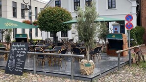 An outdoor seating area with tables and chairs, a signboard with menu items, and a building in the background. - Modern apartment in the city center of Jever (Jever)