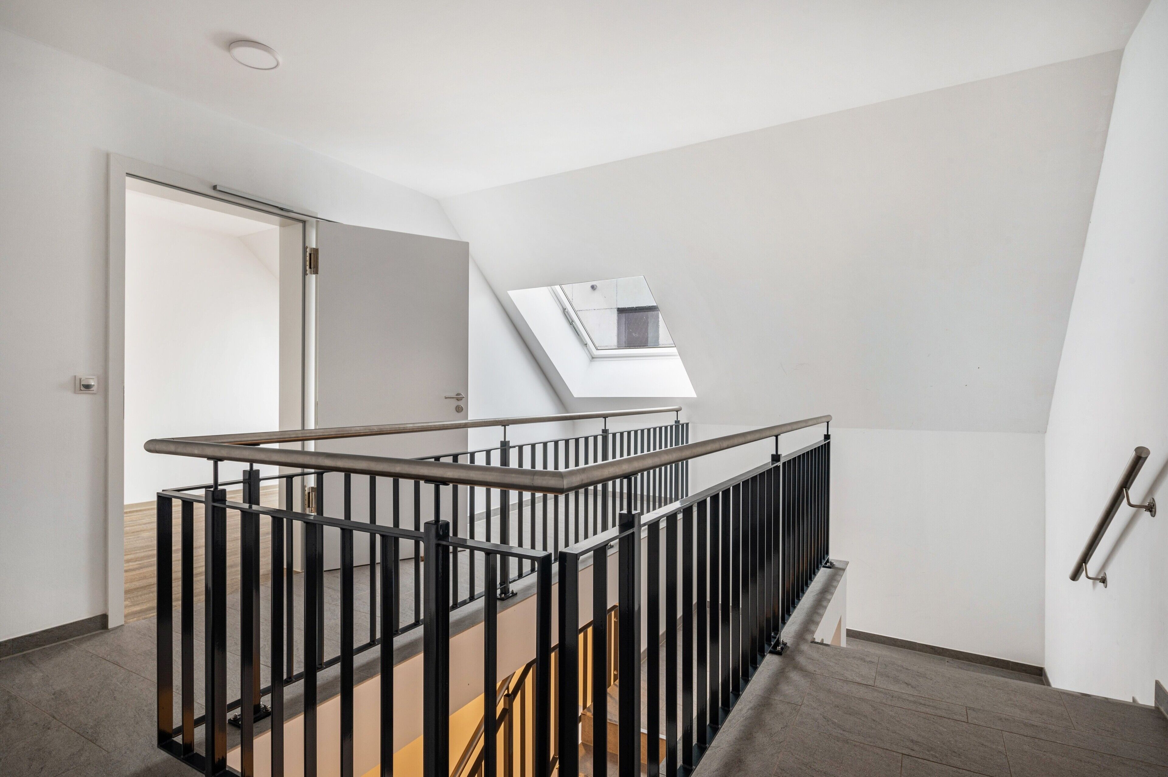 Un intérieur moderne avec un escalier, une lucarne et une porte donnant sur une autre pièce.