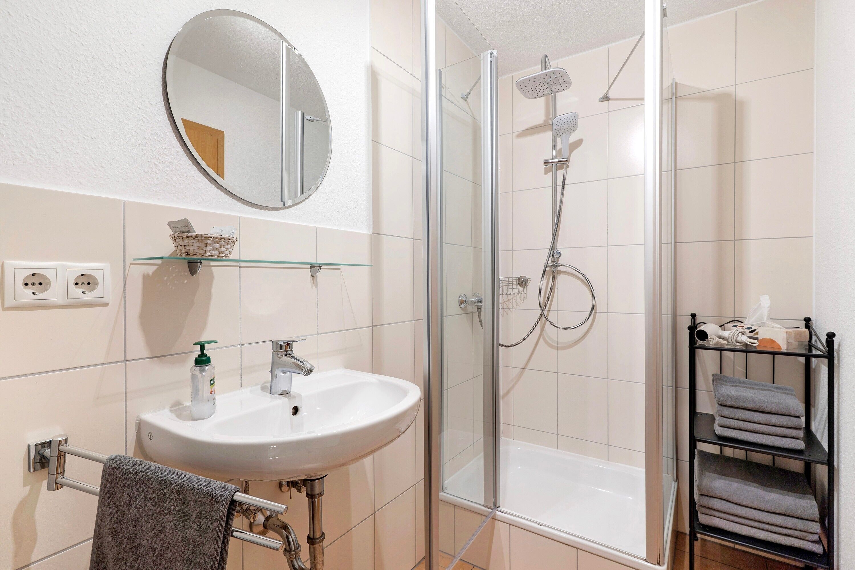 A bathroom with a glass-enclosed shower, a white sink, a mirror, and a towel rack.