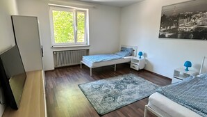Een slaapkamer met twee bedden, een radiator, een raam, een bureau en een plafondlamp.