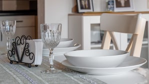Une table à manger avec des assiettes blanches et un verre transparent, un petit présentoir en métal et une chaise.