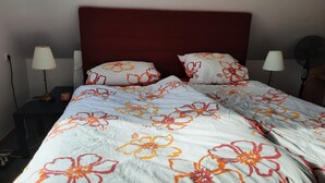 En säng med ett blommigt överkast, två sänglampor och en röd sänggavel.
