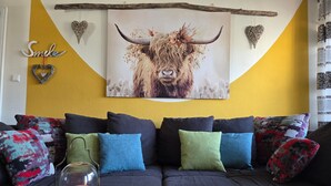 A living room with a sofa, cushions, a wall-mounted picture, and a decorative heart.