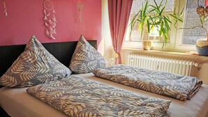 A bed with leaf-patterned bedding, a radiator, a plant, and dreamcatchers on a pink wall.