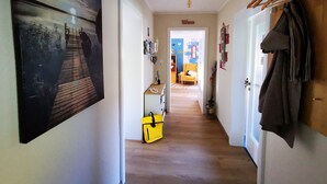 A hallway with a wooden floor, a yellow bag, a coat rack, and a door leading to a room with a bed and a blue wall.