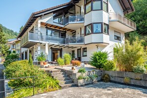 A multi-story house with a balcony, a stone staircase, and a garden.