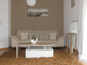 Un salon avec un canapé, une table basse, une plante en pot, un tableau accroché au mur et un rideau à motifs.