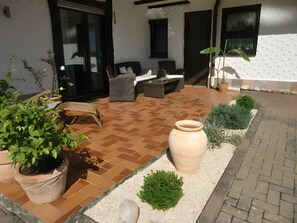 Un espace patio doté d’un sol carrelé, de mobilier d’extérieur, de plantes en pot et d’un grand vase.