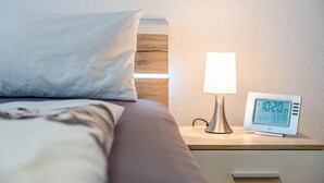 A neatly made bed with a white pillow and a bedside table with a lamp and a digital clock. - Apartment 'Ferienwohnung Uli Schätzle' with Mountain View, Private Terrace and Wi-Fi (Hornberg)