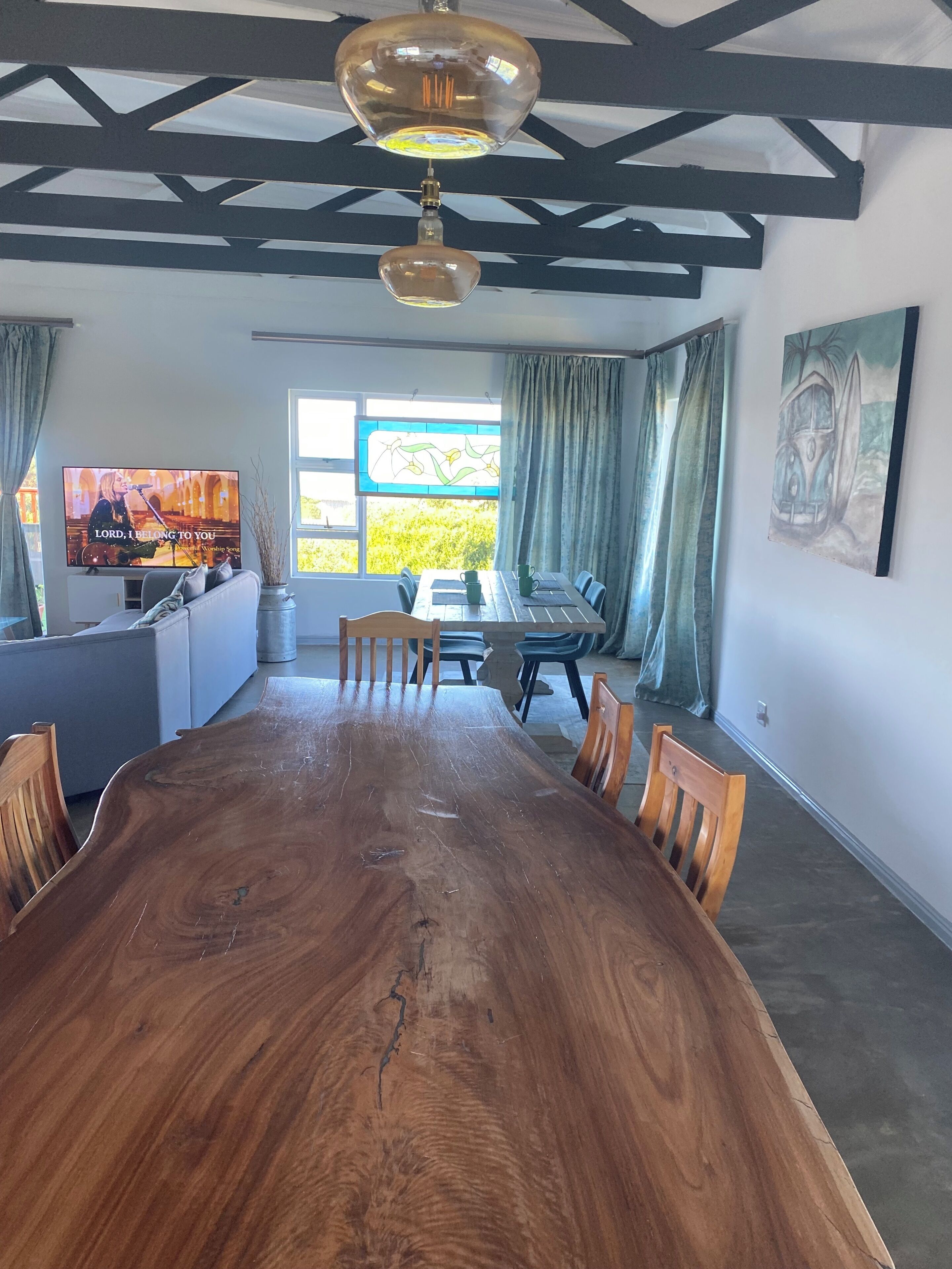 A dining area with a long wooden table, chairs, a television, and a window with curtains.