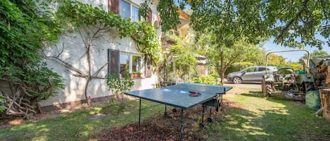 A courtyard with a ping pong table, a car, and a building with a sloped roof.
