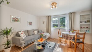 A living room with a sofa, a coffee table, a dining table with chairs, a potted plant, and a window with curtains. - Apartment 'Haus Zur Bienenweide' with Shared Terrace, Balcony and Wi-Fi (Schömberg)