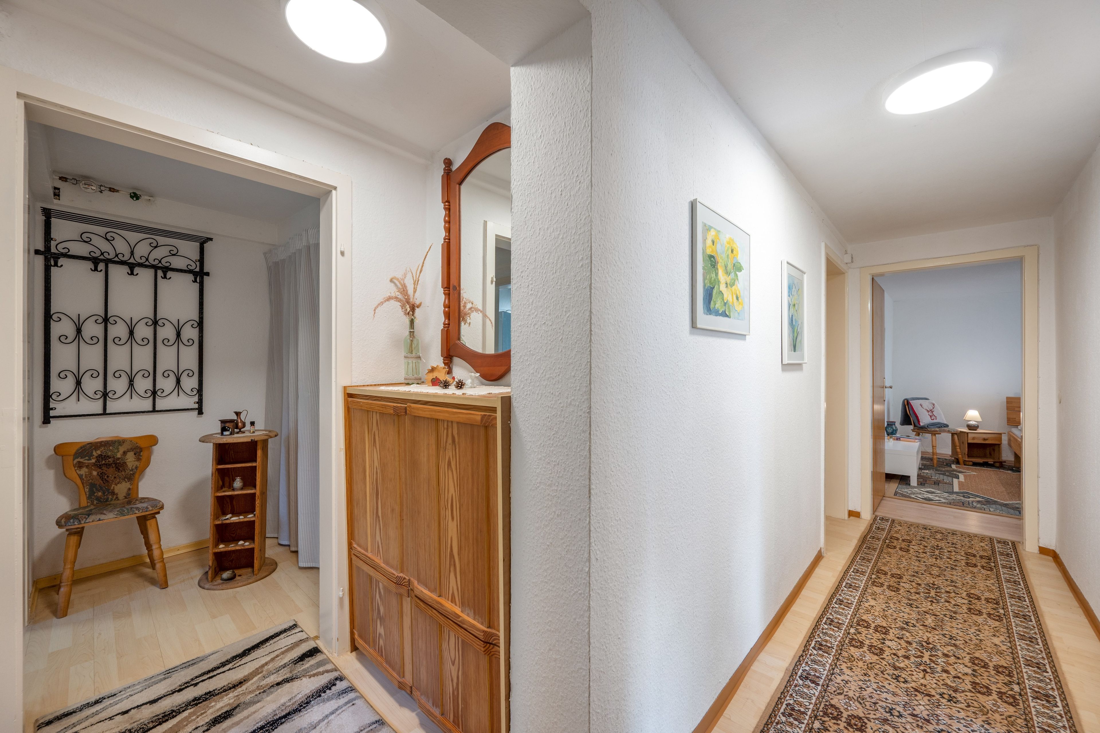 Ein Korridor mit einem Holzschrank, einem Sessel, einem Spiegel und einem Teppich mit Muster.