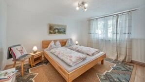 A bedroom with a wooden bed, two bedside tables with lamps, a painting on the wall, and a window with curtains. - Apartment 'Haus Zur Bienenweide' with Shared Terrace, Balcony and Wi-Fi (Schömberg)