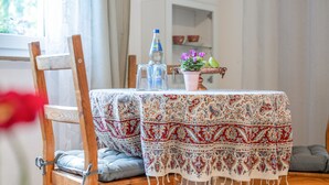 A dining area with a table covered by a patterned tablecloth, a chair with a cushion, a bottle of water, a glass pitcher, and a potted plant with purple flowers. - Apartment 'Haus Zur Bienenweide' with Shared Terrace, Balcony and Wi-Fi (Schömberg)