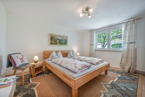 Un dormitori amb un llit de fusta, una tauleta de nit, una làmpada, un quadre a la paret i una finestra amb cortines.