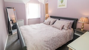 A bedroom with a large bed, a bedside table, a lamp, a mirror, and a window. - Medical Hall (Cemaes Bay)