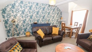 A living room with a brown leather sofa, a round wooden coffee table, and a patterned wall. - Medical Hall (Cemaes Bay)