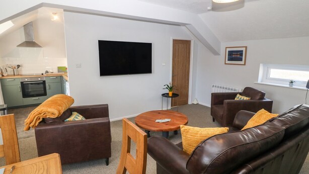 A modern living room with a brown leather sofa, a wooden coffee table, and a television mounted on the wall. - Medical Hall (Cemaes Bay)