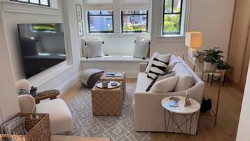 A cozy living room with a sofa, a coffee table, a TV, and a window seat with cushions.
