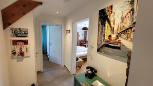 A hallway with a bed, a telephone, and a painting of a street scene. - Apartment 'Schwarzwald-Traum' with Mountain View, Private Terrace and Wi-Fi (Haslach im Kinzigtal)