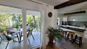 A modern kitchen with a large island, a dining area with a table and chairs, and a sliding glass door leading to a patio with a view of greenery. - Apartment 'Schwarzwald-Traum' with Mountain View, Private Terrace and Wi-Fi (Haslach im Kinzigtal)