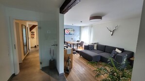 A modern living room with a grey sofa, a dining area with a table and chairs, a hallway leading to another room, and a ceiling fan. - Apartment 'Schwarzwald-Traum' with Mountain View, Private Terrace and Wi-Fi (Haslach im Kinzigtal)