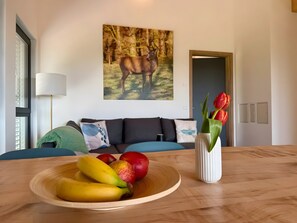 A dining table with a fruit bowl, a vase with tulips, a sofa, and a painting of a deer.