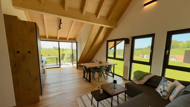 A spacious loft with a dining area, a sofa, and large windows offering a view of the countryside. - Holiday Apartment 'Spatzennest' with Mountain View, Balcony and Wi-Fi (Dachsberg (Südschwarzwald))