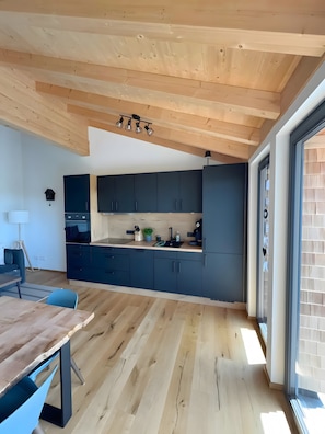 A modern kitchen with dark cabinets, a wooden ceiling, and a large window.