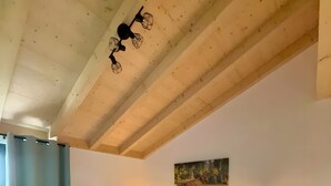 A bedroom with a wooden ceiling, a bed with white linens, two bedside tables with lamps, and a painting on the wall. - Holiday Apartment 'Spatzennest' with Mountain View, Balcony and Wi-Fi (Dachsberg (Südschwarzwald))