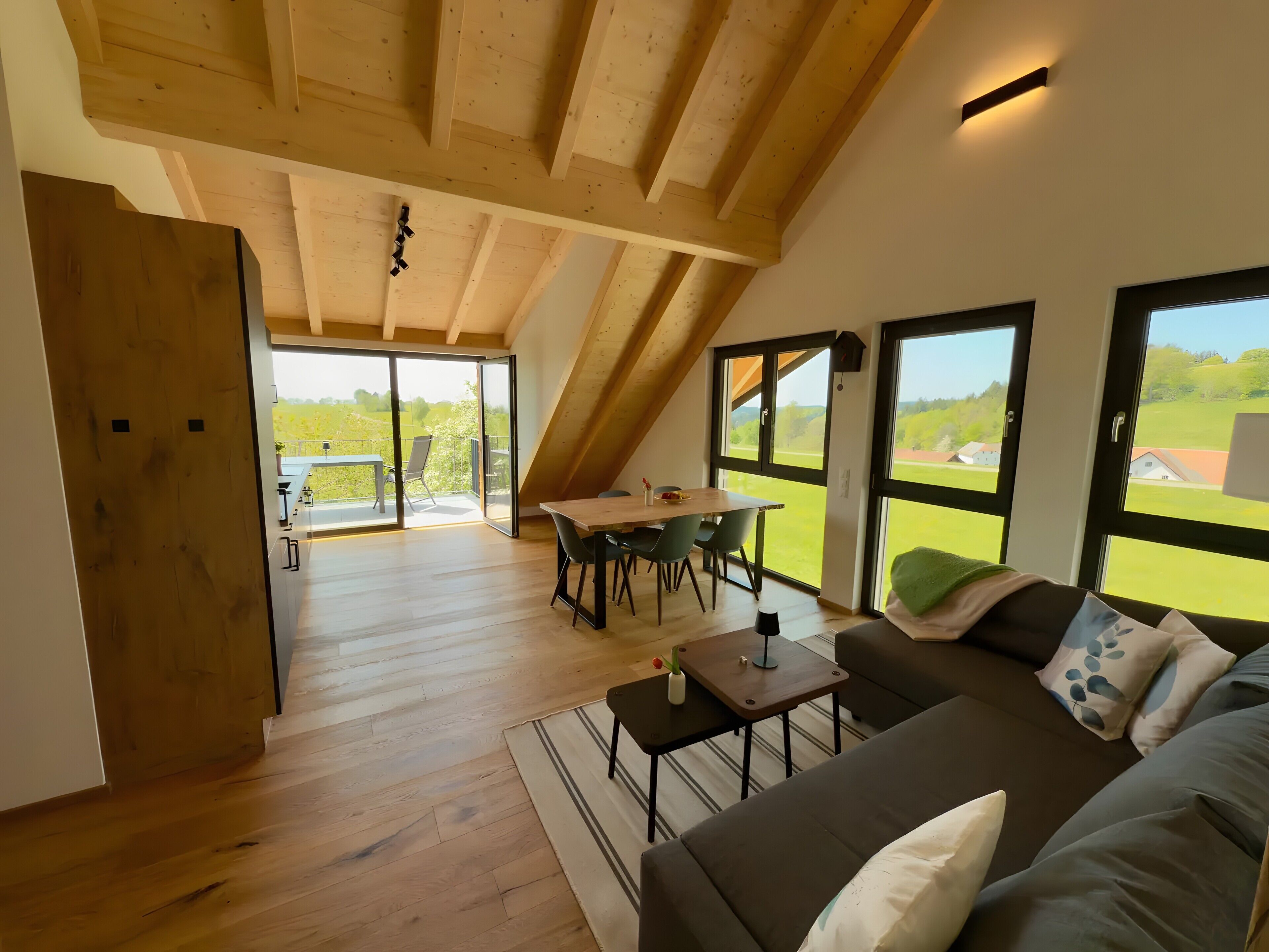 Un loft espacioso con comedor, sofá y grandes ventanales que ofrecen vistas al campo.