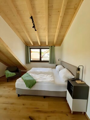 A bedroom with a bed, a nightstand, a lamp, a chair, and a window with curtains.