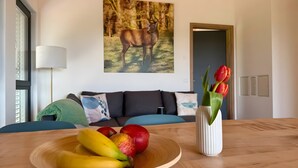 A dining table with a fruit bowl, a vase with tulips, a sofa, and a painting of a deer. - Holiday Apartment 'Schwalbennest' with Mountain View, Balcony and Wi-Fi (Dachsberg (Südschwarzwald))