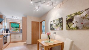 Cocina moderna con armarios de madera, una mesa de comedor con sillas y vistas al jardín a través de una puerta abierta.