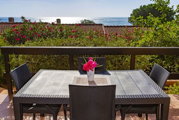 A patio with a table and chairs, a vase with flowers, and a view of the sea.