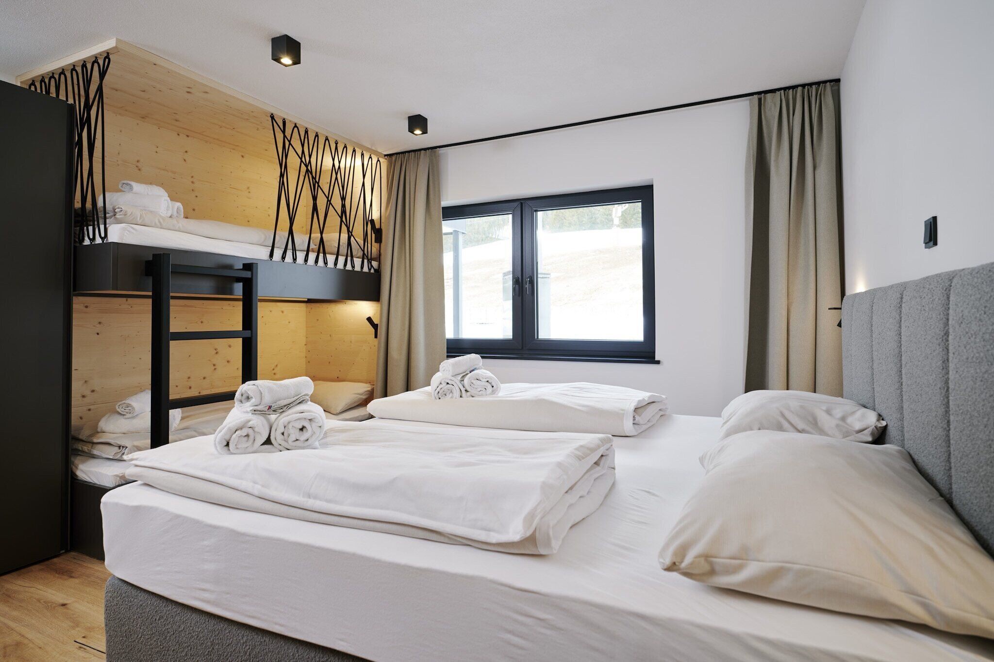 A modern hotel room with a bunk bed, a desk, and a large window.