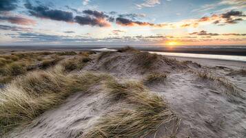 Een zandstrand met duinen en een ondergaande zon.