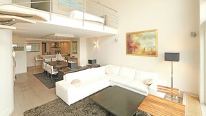 Un apartamento moderno con comedor, sala de estar con sofá y mesa de centro, y balcón con barandilla.