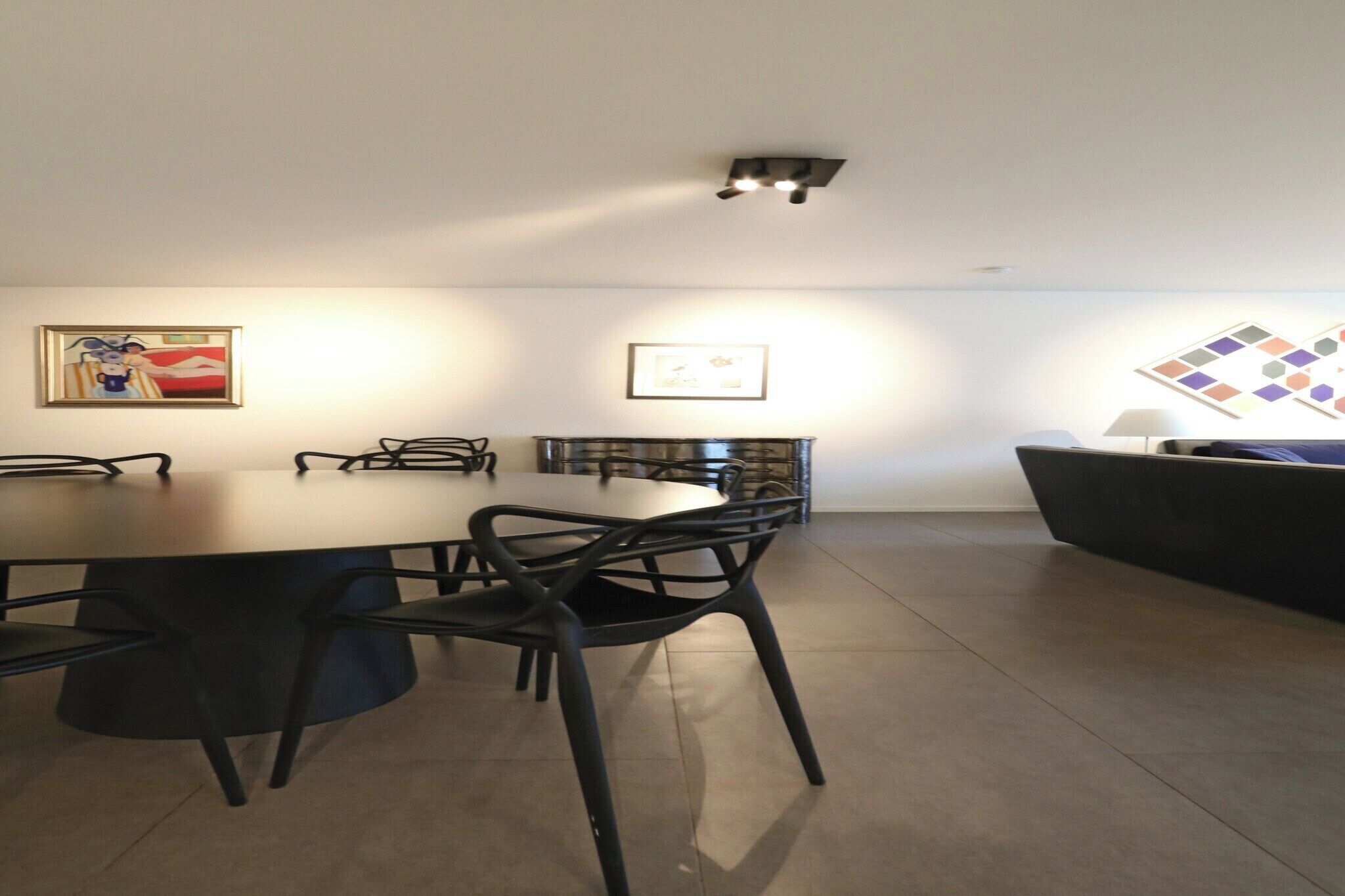 A modern dining area with a round table and black chairs, a sofa, and framed artwork on the walls.