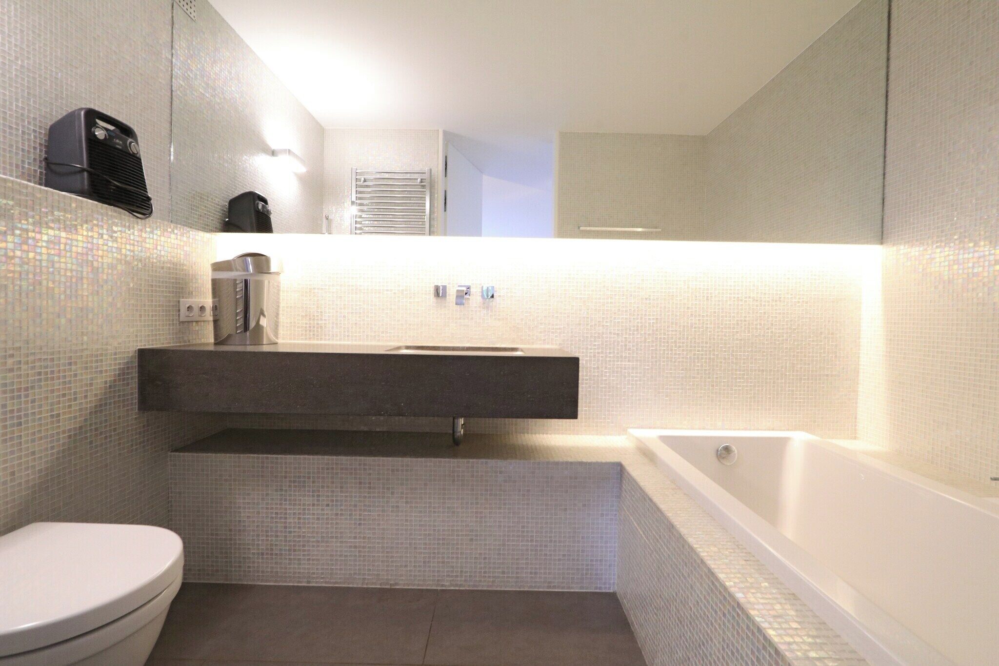 Une salle de bain moderne avec des toilettes blanches, un lavabo avec un miroir au-dessus et une baignoire.
