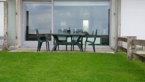 Une terrasse avec une table et des chaises, une porte-fenêtre coulissante et une pelouse verdoyante.