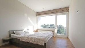 Une chambre à coucher avec un lit, une table de chevet, une fenêtre donnant sur un beau paysage et un luminaire au plafond.