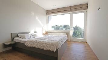 Une chambre à coucher avec un lit, une table de chevet, une fenêtre donnant sur un beau paysage et un luminaire au plafond.