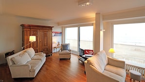 Een ruime woonkamer met een groot raam, een houten kast en een beige bank.