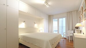 Een slaapkamer met een groot bed, een bureau en een stoel. Er zijn kastjes en een raam met gordijnen.