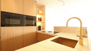 Eine moderne Küche mit Holzausstattung, einem schwarzen Backofen, einer Spüle mit Goldarmatur und einer Marmorarbeitsplatte.